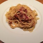 Piatto di carbonara con guanciale, spaghetti e tuorlo d'uovo, evidenziando un errore comune nella preparazione.