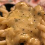 Pasta ai 4 formaggi con una salsa cremosa e filante, servita in un piatto bianco.